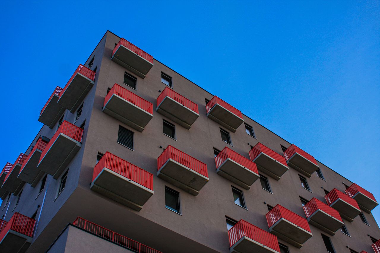mission-img Low-angle view of a Vienna residential building with red balconies against a clear blue sky.