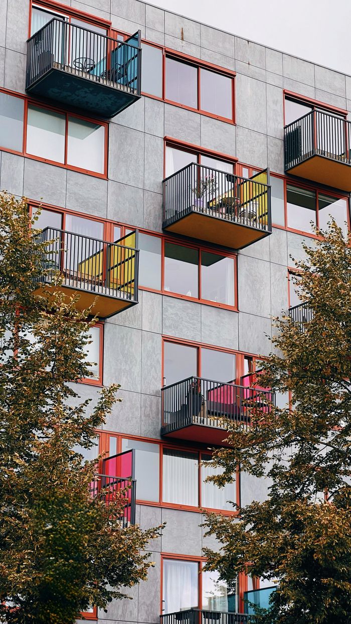 testimonials-img Vertical view of a modern residential block with colorful balconies and trees.