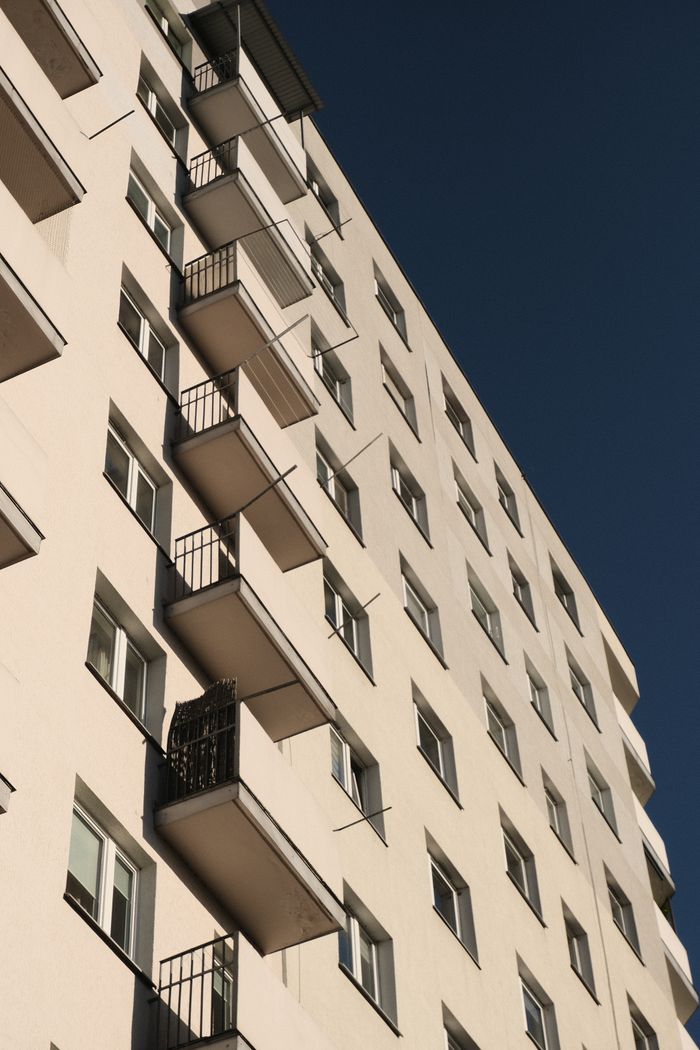 home-services-004 Close-up view of a modern urban residential building with multiple balconies under a clear blue sky.